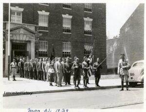 Group of men, some in uniform processing out of a building.
